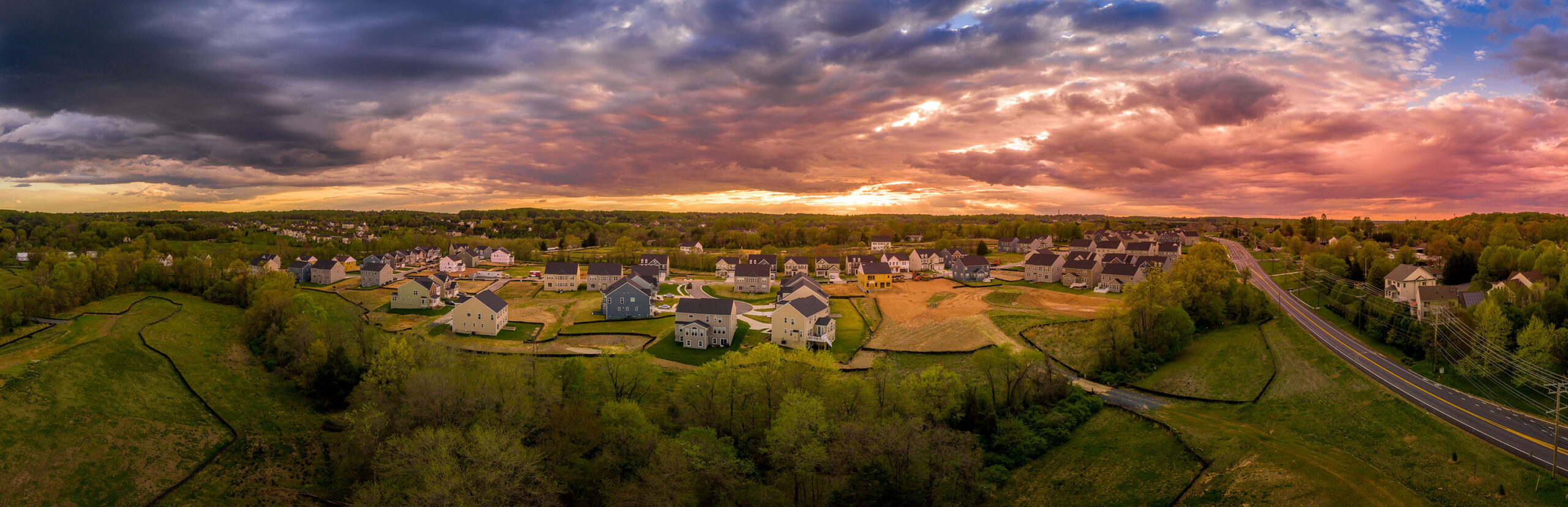 Aerial sunset panorama of luxury real estate development single family house neighborhood street with dramatic sky